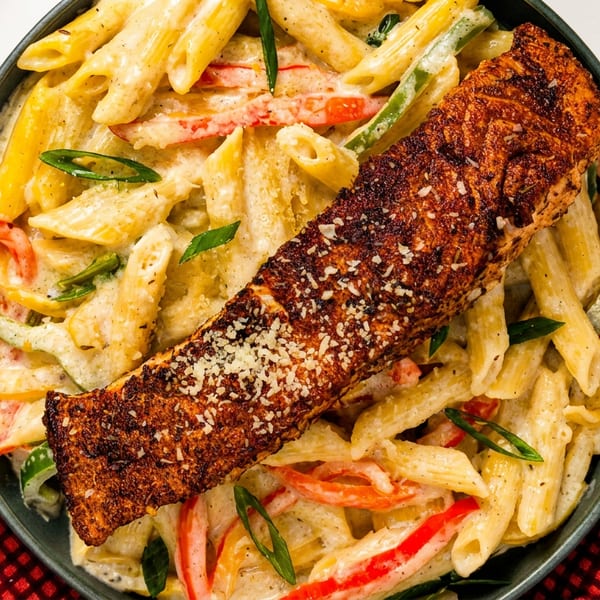 Creamy penne pasta with colorful bell peppers, topped with a seasoned salmon fillet and parmesan.