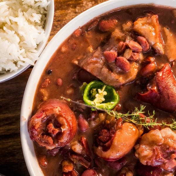 A bowl of red beans and rice with pork, green peppers, and thyme on a wooden table.