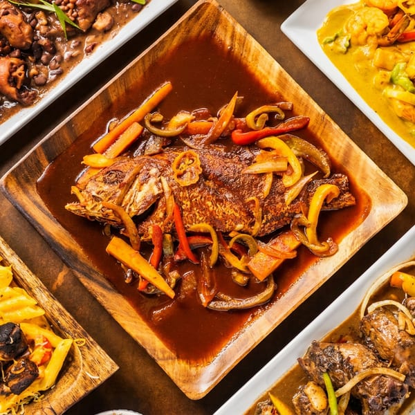 Assortment of Caribbean dishes, including whole fried fish, curried shrimp, oxtail, and mac and cheese.